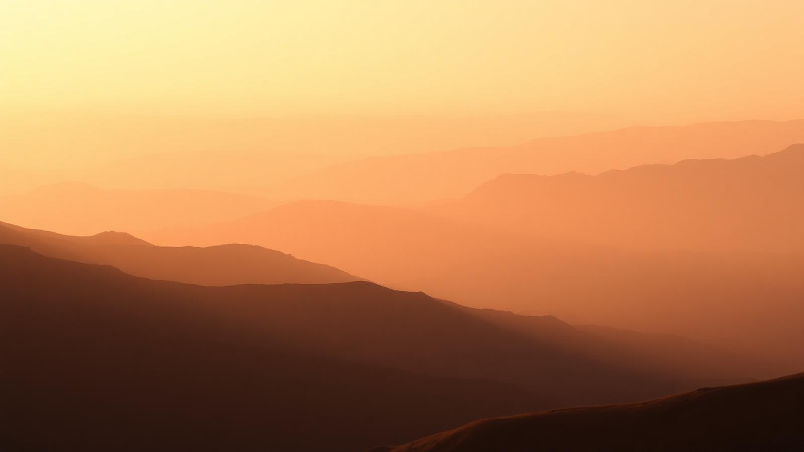 Layered mountain ridges at sunrise in warm haze